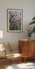 a cozy living room with a wooden cabinet, a beige armchair, a framed picture of pink flowers, and a potted plant.