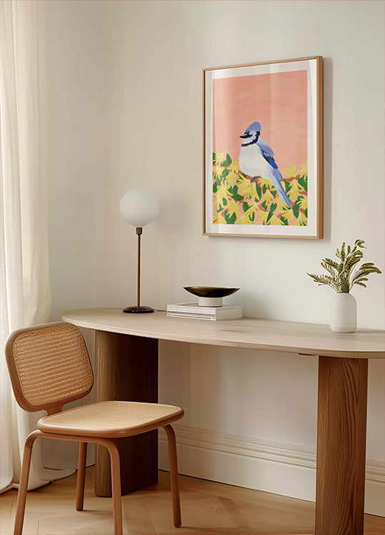 a cozy corner of a room with a wooden desk, a woven chair, a lamp, and a framed picture of a blue bird on a yellow background.